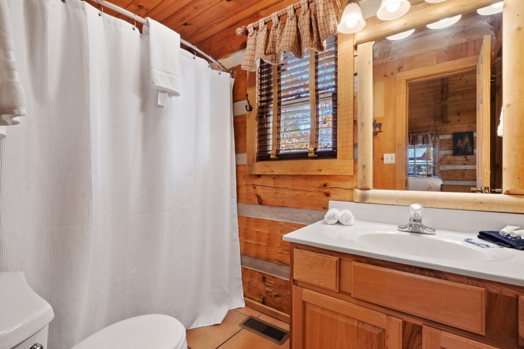 Bathroom at Nestled Oaks cabin in Sevierville TN featuring wood-paneled walls, a white shower curtain, and rustic vanity mirror.
