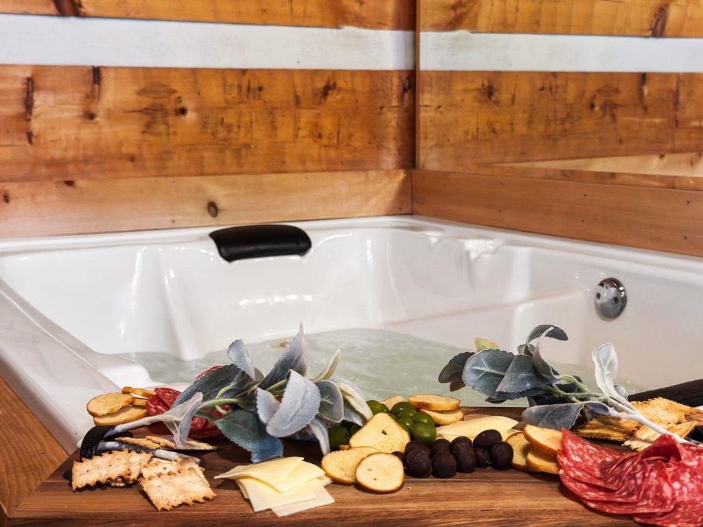 Indoor jetted tub at Nestled Oaks cabin in Sevierville TN with charcuterie board and rustic wood walls.
