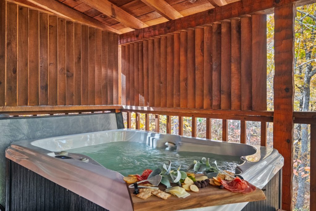 Private outdoor hot tub at Nestled Oaks cabin in Sevierville TN with charcuterie board and forest backdrop.